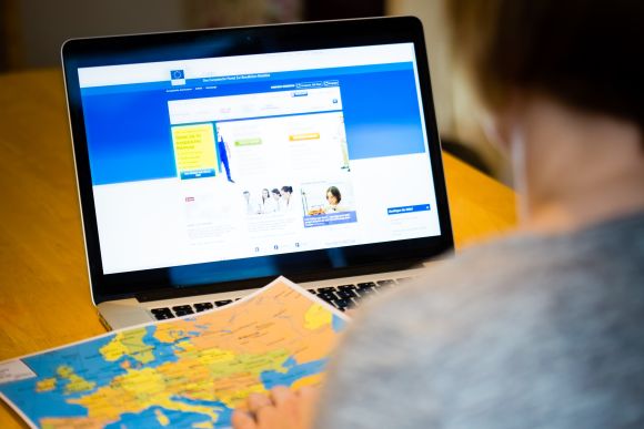 Finding employment opportunities across Europe: a woman using the EURES online portal to find a job abroad, while looking to a map of Europe